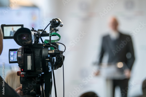 TV camera filming live press event with officials at podium. Highlights media coordination, lighting precision, and structured public communication.