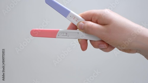 A woman's hand holding two positive pregnancy tests on gray background.