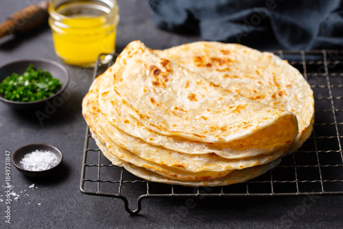 Billede på lærred Flaky golden flatbreads cooling on rack, garnished with herbs, salt, and ghee, artisanal food presentation