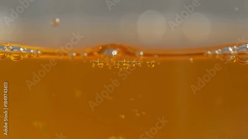 Macro close up of refreshing golden liquid with bubbles rising and popping in a glass.