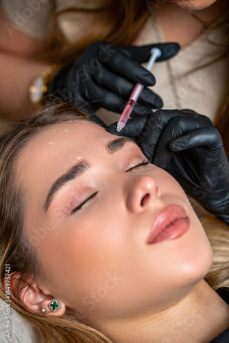 Beauty injection. Hand with syringe doing hyaluronic puncture. Cosmetic treatment. Young woman receiving filler injection in forehead. Beautician expert's hands injecting botox in female forehead