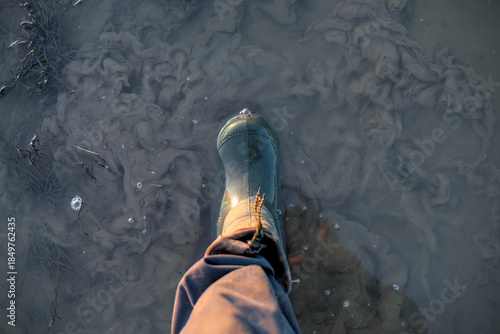 Top view of foot in green rubber boot in a puddle