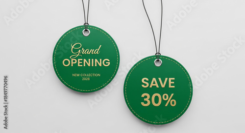 Two green round tags with gold text, suspended by strings. Text announces grand opening and discount offer, representing retail promotion.