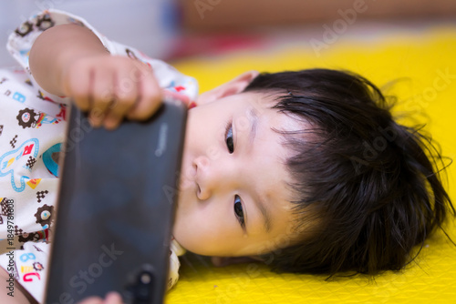 A close-up of a young Asian boy with a tear in his eye while staring at a smartphone. Concept of digital eye strain, emotional impact of social media on children, and early screen time concerns.