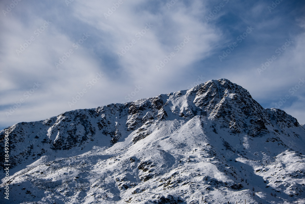 Obraz premium Snow-covered mountain ridge under dramatic cloudy sky. Winter alpine landscape with rugged peaks and natural textures.
