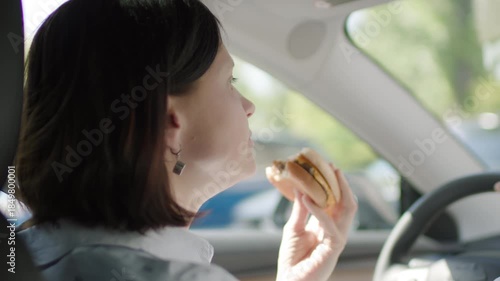 Woman eating a burger behind the wheel, showing distracted driving and road safety risk.