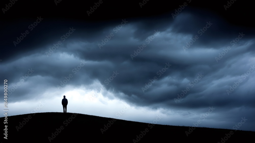 Fototapeta premium Man standing alone on a dark hill with a foreboding sky, representing depression, solitude, and difficult times