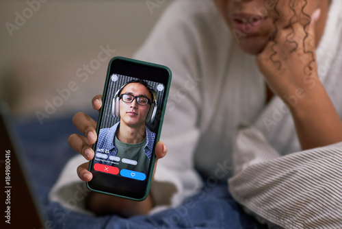 Wallpaper Mural Young adult Black woman holding smartphone showing dating app profile of young Asian wearing glasses, lying on bed, engaging in online dating activity Torontodigital.ca