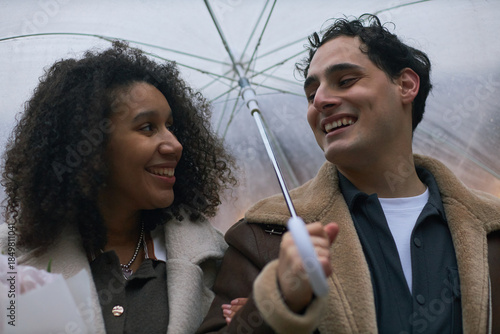 Foto Young adult Caucasian man and young adult Black woman smiling and walking closel