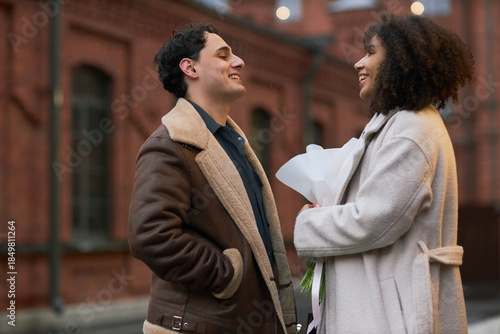 Tableau sur toile Young adult Caucasian man smiling and talking with young adult Black woman holdi