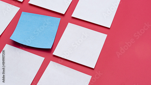 Fotografía Grid of White Square Papers with One Unique Blue Note on Red