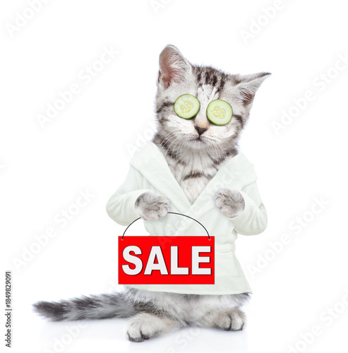 Cute kitten with slices of cucumber on it eyes wearing bathrobe with towel on it head holding signboard with labeled 