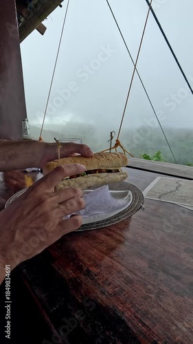 Preparing to eat a sub sandwich while enjoying the view of the foggy forest in the distance from a wooden balcony