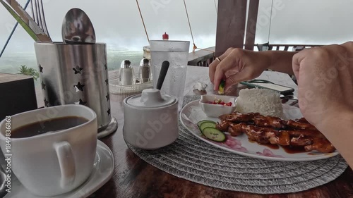 Candid low angle view of hand squeezing calamansi on a saucer with chopped chili to make traditional condiment for pork barbecue skewers, enjoying local Filipino meal