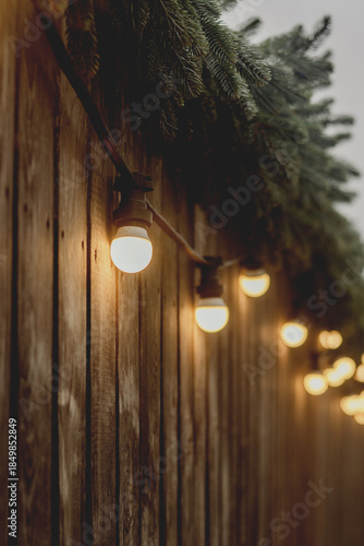 Warm String Lights on Wooden Fence with Evergreen Decor
