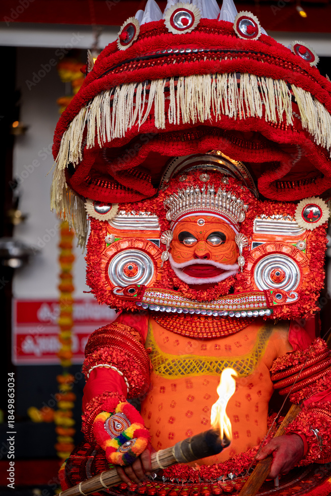 Fototapeta premium Kannur, Kerala / India – December 12, 2025: A Theyyam performer dressed in traditional red ritual costume holds a flaming torch during a Theyyam ritual performance at a temple in Kannur district