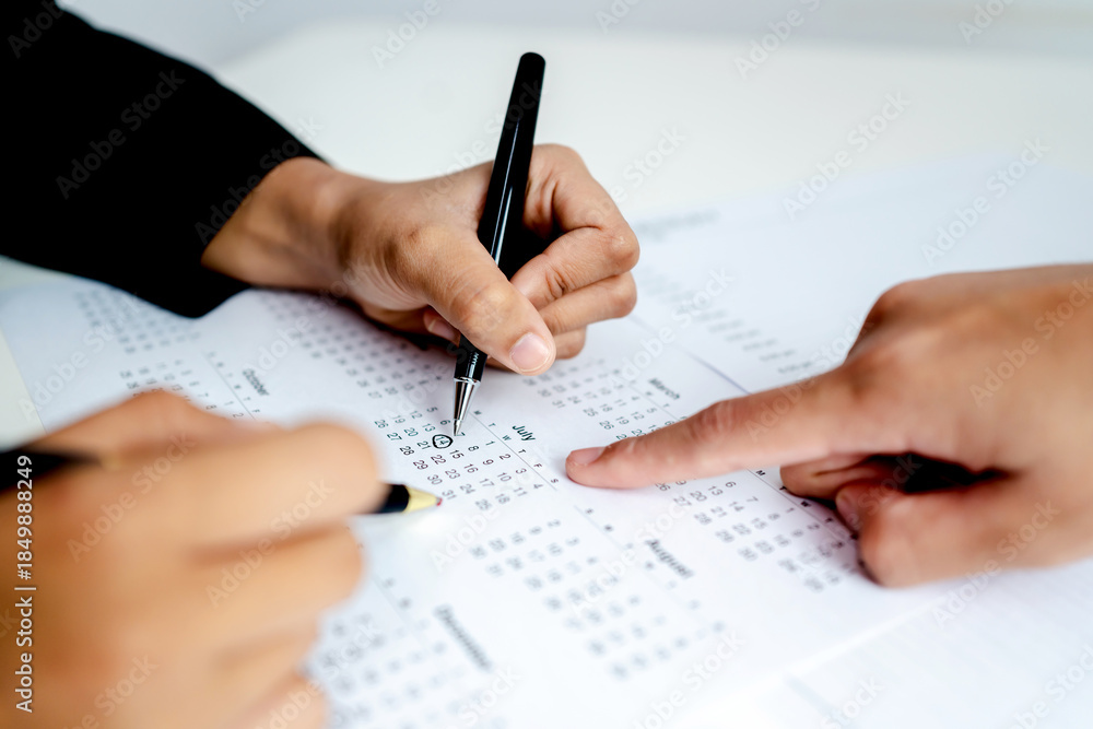 Naklejka premium Close up of business people marking dates on calendar with pen and finger, planning schedule, deadline management, teamwork, meeting and time management concept.