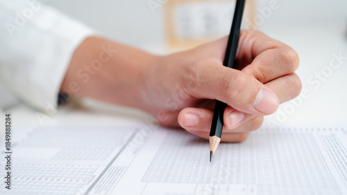 Close up of hand filling answer sheet with pencil, multiple choice test form, exam assessment, survey evaluation and education or research concept.