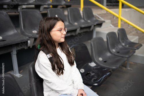 Happy teenage girl with backpack sitting at football stadium, exploration learning and vacation concept