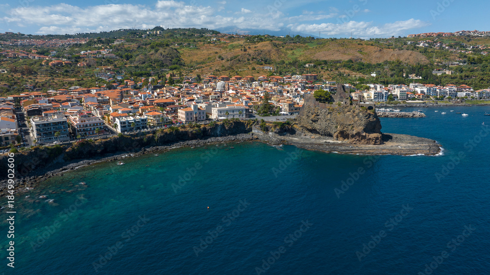 Fototapeta premium Panoramic aerial view of Aci Castello, a coastal village overlooking the Ionian Sea, in the province of Catania, Sicily, Italy. In the foreground is the castle, the town's symbol and attraction.