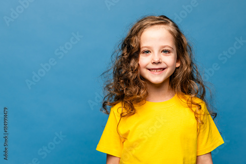 Close-up portrait of nice-looking pretty cute lovely attractive cheerful cheery content long-haired little girl in yellow t-shirt isolated over vibrant blue color background