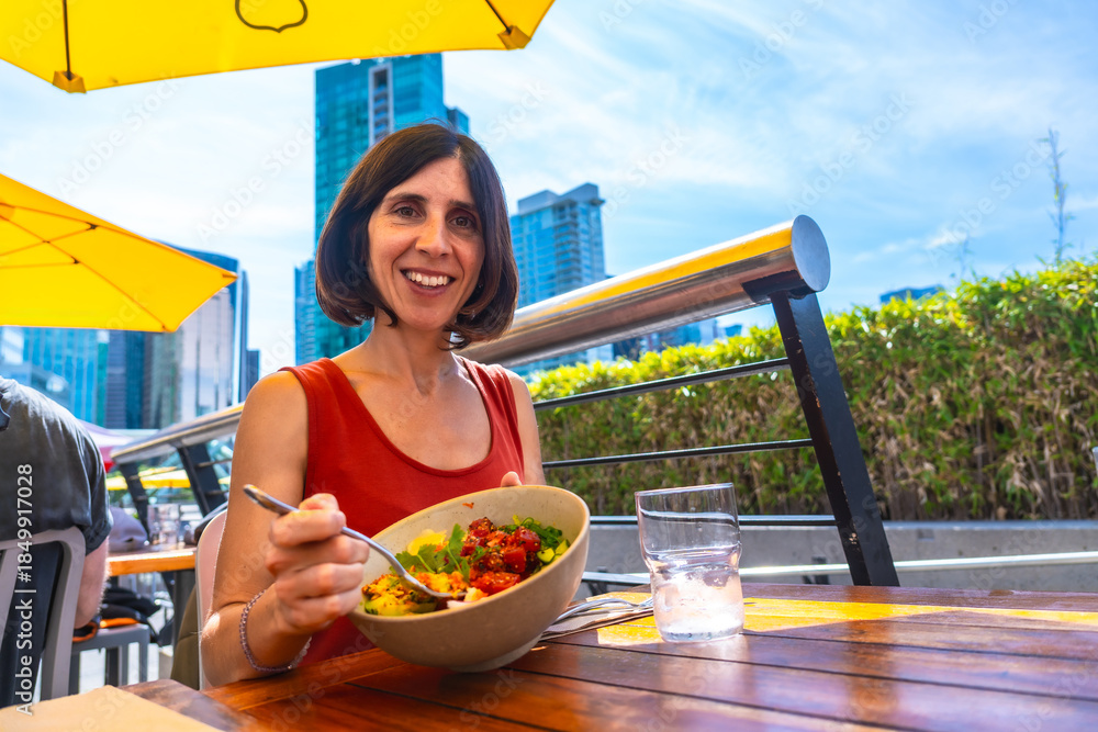 Obraz premium Woman eating healthy poke bowl in vancouver restaurant patio