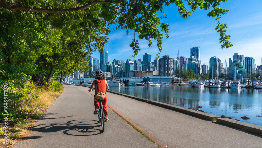 Fototapeta premium Woman cycling in stanley park with vancouver skyline in background
