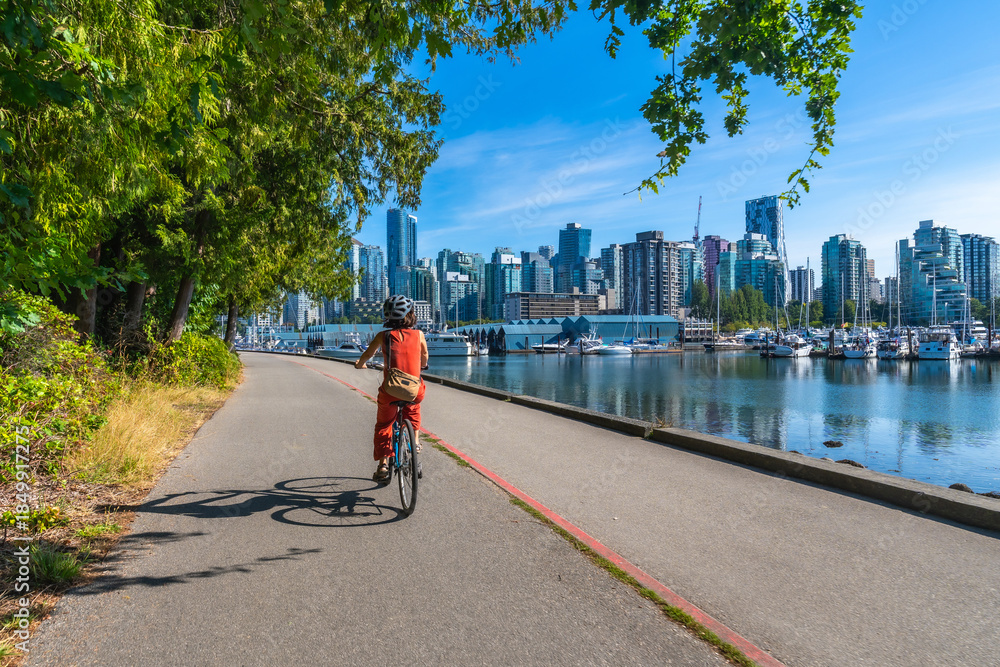 Fototapeta premium Tourist riding bicycle in stanley park with vancouver skyline in background