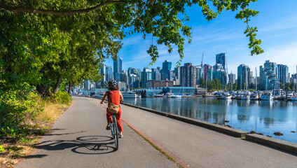 Woman cycling in stanley park with vancouver skyline in background