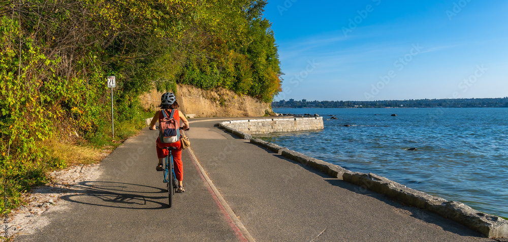Fototapeta premium Woman cycling along stanley park seawall in vancouver, british columbia
