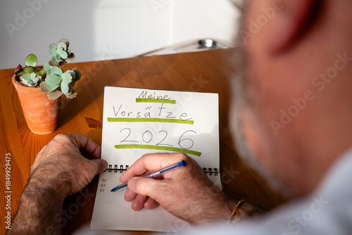 Mann schreibt Vorsätze für 2026 in Notizbuch am Holztisch