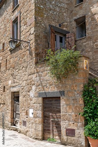  Italy - Bagnoregio - Civita di Bagnoregio - Rustic stone house corner with shuttered windows, wooden balcony, lantern and climbing greenery