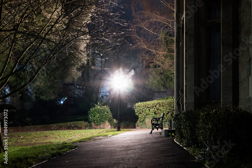A bench and park next to Victorian gothic building. converted into offices on a winters night. Malvern UK