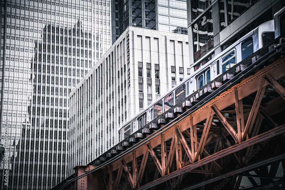 Naklejka premium Dramatic view of the iconic Chicago L elevated train and rusted tracks against a backdrop of modern, vertical skyscraper windows. Urban contrast and infrastructure.