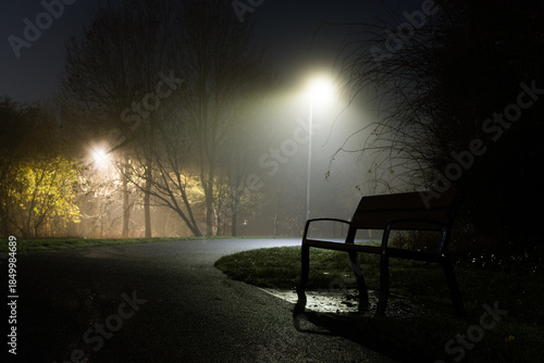 A bench in a park on a quiet foggy winters night in a park