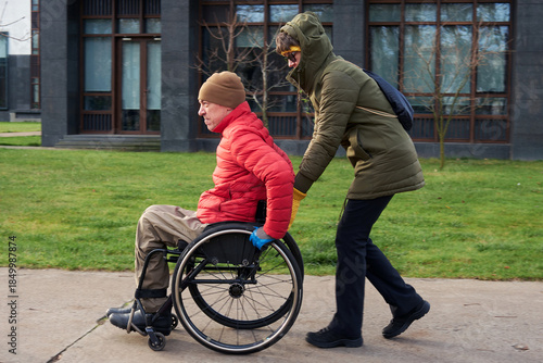 Photos A man in a wheelchair is riding on the sidewalk while a woman is helping him