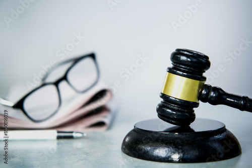 Stack of newspapers, black judge's gavel and glasses on the desk.