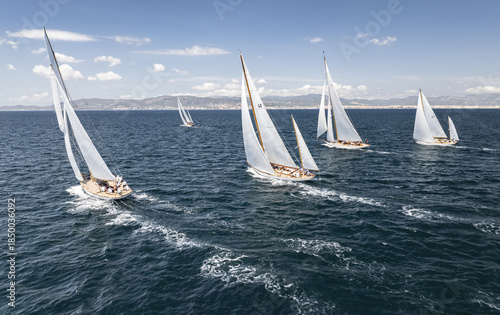 Palma, Spain - 17 August 2024: Aerial view of sailboats gliding across the turquoise waters, their white sails billowing against the distant cityscape.