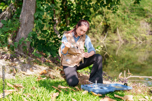 Asian adult woman environmental scientist conducts water quality testing collecting samples during fieldwork by riverbank studying ecology