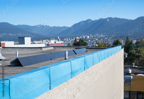 Roof metal flashing installation on flat roof with defocused city and mountains. 2-ply SBS or modified bitumen roofing repair. Waterproof membrane and sheet metal corner installation. Selective focus.