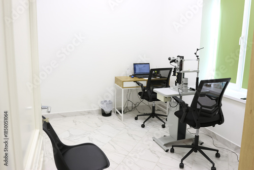 Interior of an ophthalmologist's office with a slit lamp biomicroscope, a table with a laptop in a bright and clean medical examination room.
