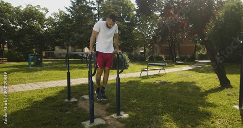  Young athlete performs dips exercise on parallel bars in park, street workout, slow motion