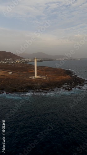 Vertical High Altitude Drone Shot over Atlantic Ocean Flying Inland Towards Faro de Pechiguera Lighthouse and Volcanic Coast of Lanzarote