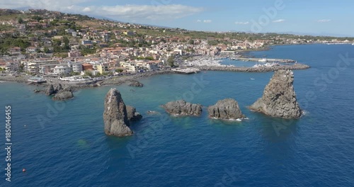 Aerial view of the town of Aci Trezza overlooking the Ionian Sea, in province of Catania, Sicily, Italy. In the foreground, off the coast, there are three tall, characteristic and prominent sea stacks