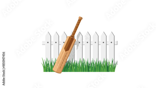 A cricket bat leans against a white picket fence with lush green grass growing in front, creating a peaceful outdoor scene.