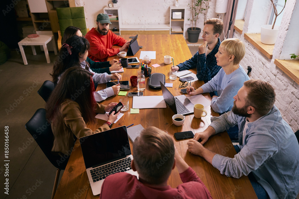 Obraz premium Creative team meeting viewed from above in modern office. Concept of strategic discussion, collaborative planning, teamwork dynamics and contemporary coworking business environment.