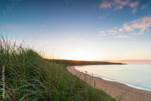 Melvich Bay. Scotland, NC500 route. Golden sunset over calm beach with dunes and grass at the horizon