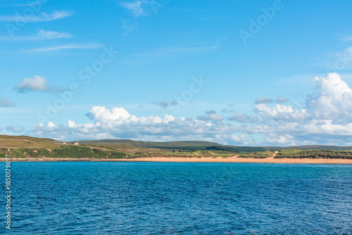 Melvich Bay. Scotland, NC500 route. Calm coastal seascape with blue water, sandy beach, and open sky under bright clouds above