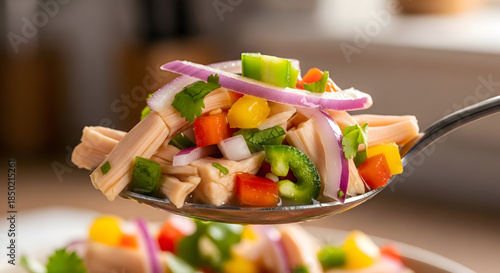 Spoonful of colorful ceviche on a blurred background with a plate in the background