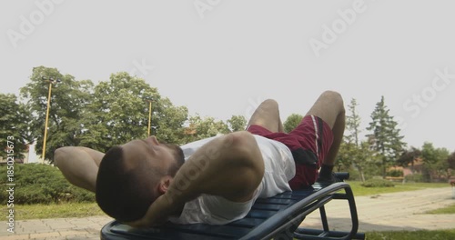 Young male fit athlete doing abs exercise on bench, street workout concept, slow motion